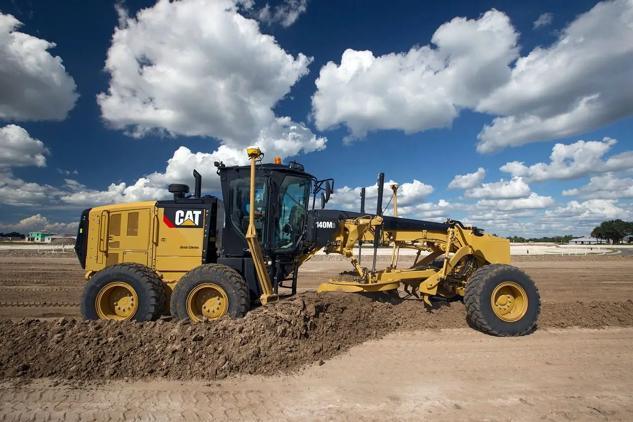 Cat motor grader on a dirt surface under a blue sky