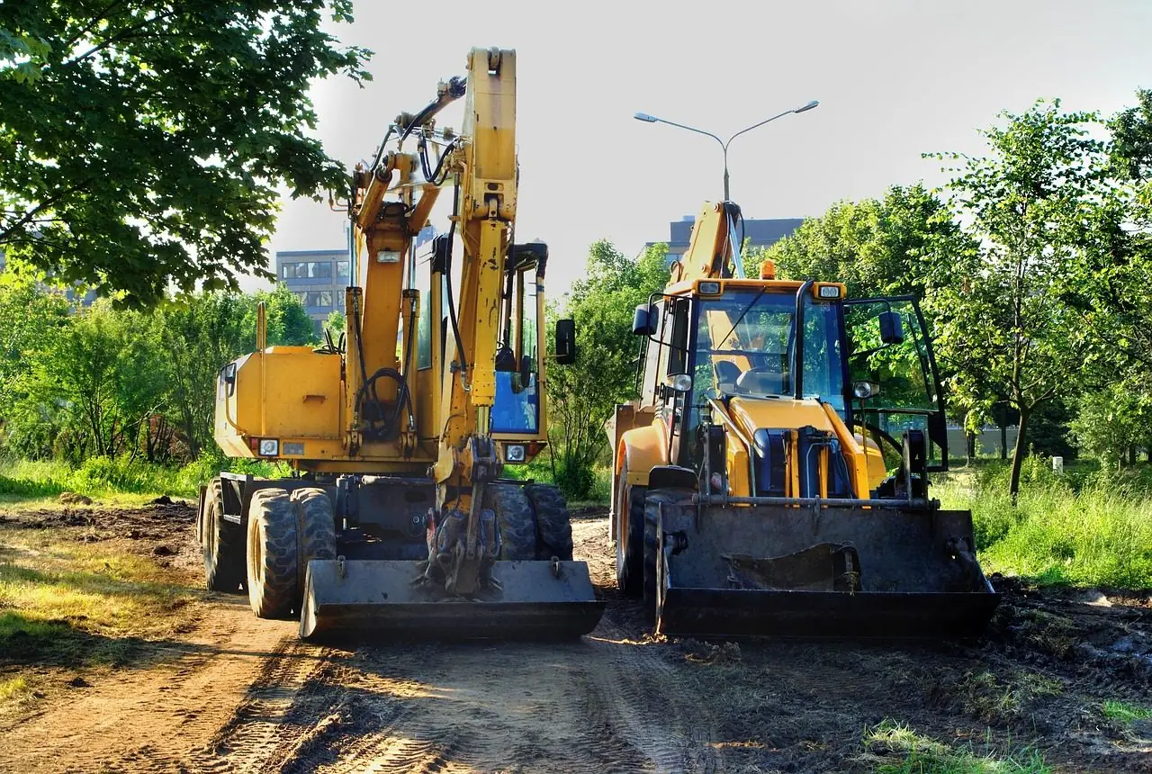 Two yellow wheeled excavators on a dirt road beside trees
